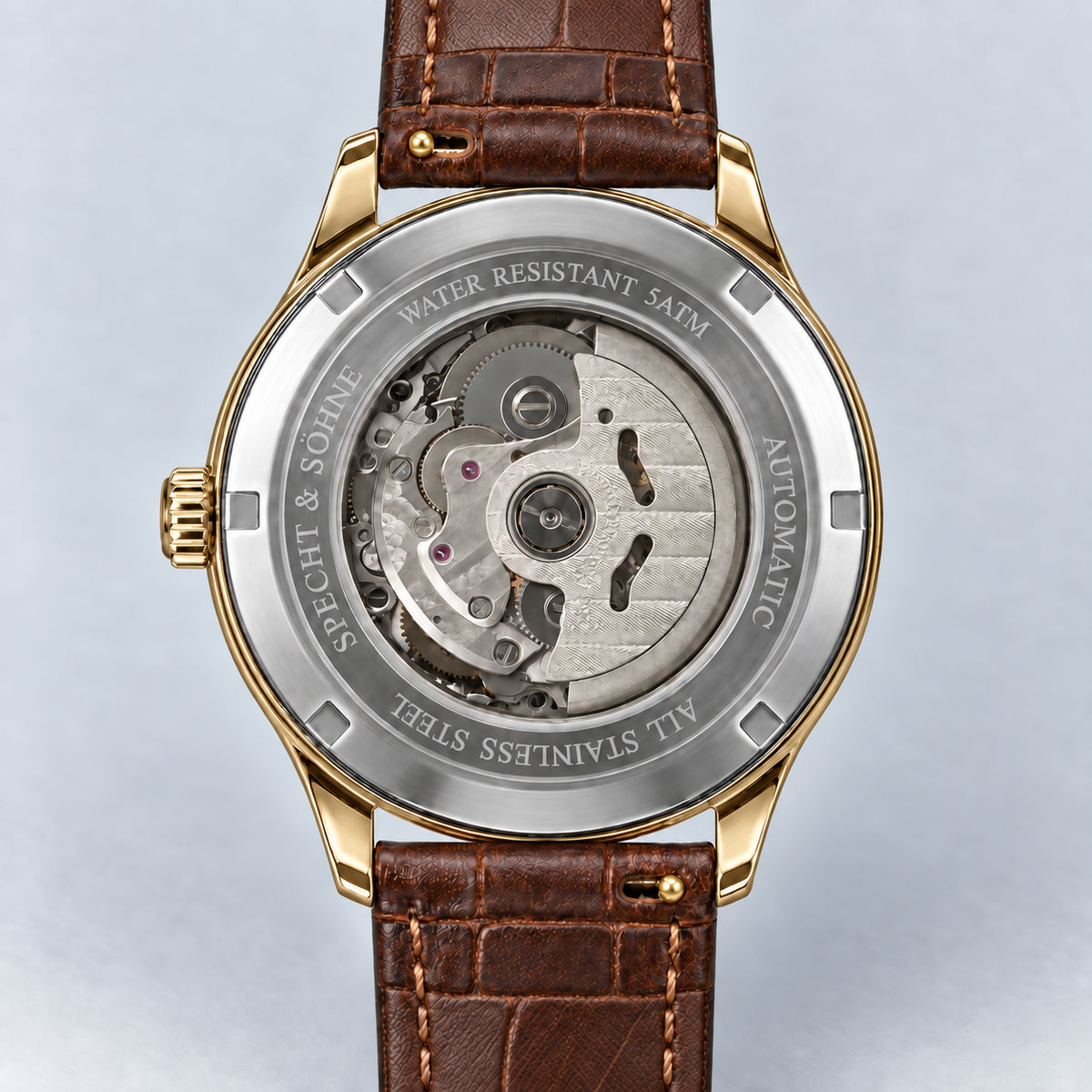 Verso do Specht & Söhne Invictus 1986 Gold, com tampa prateada, movimento visível, laterais e encaixes dourados e pulseira marrom.