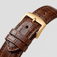 Pulseira marrom do Specht & Söhne Invictus 1986 Gold com textura, costura e fivela de pino dourada sobre fundo claro.